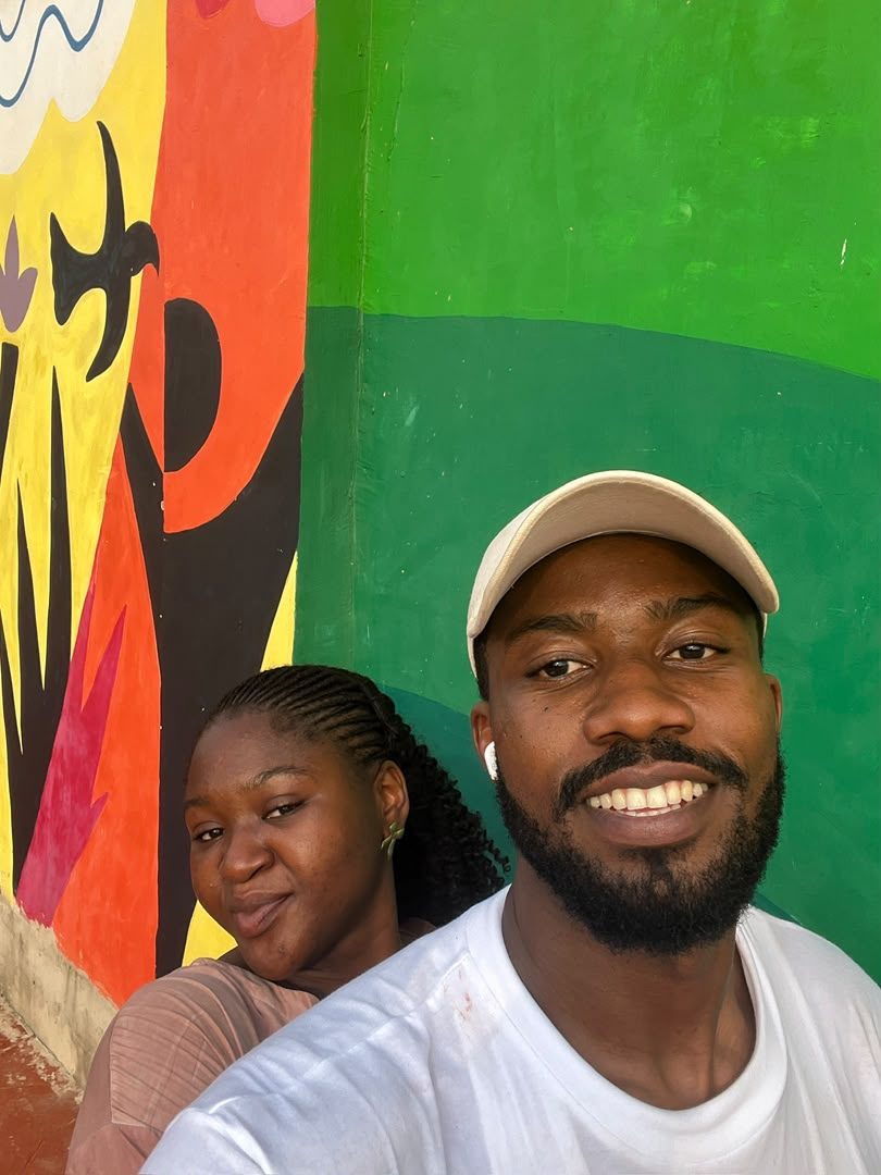 Chukwuma in a cap with Nnenna behind him, in front of a bright mural